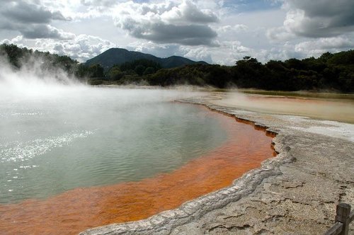 Steaming geothermal pool rimmed with orange mineral deposits near Rotorua